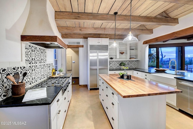 kitchen with a center island, custom range hood, appliances with stainless steel finishes, beam ceiling, and butcher block counters