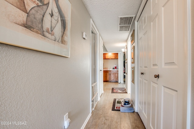 hallway featuring a textured ceiling and light hardwood / wood-style flooring