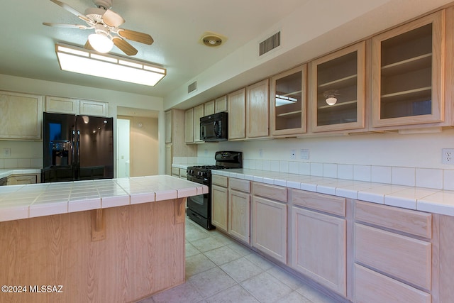 kitchen with light brown cabinets, tile countertops, black appliances, light tile patterned floors, and ceiling fan