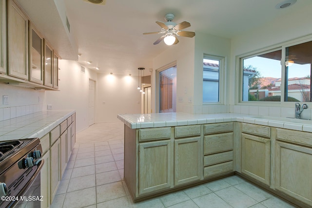 kitchen with tile counters, stainless steel range, hanging light fixtures, kitchen peninsula, and light tile patterned flooring