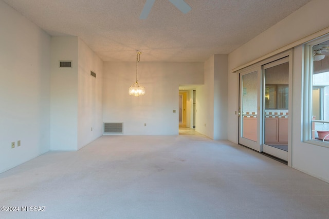 carpeted spare room featuring a textured ceiling and ceiling fan with notable chandelier