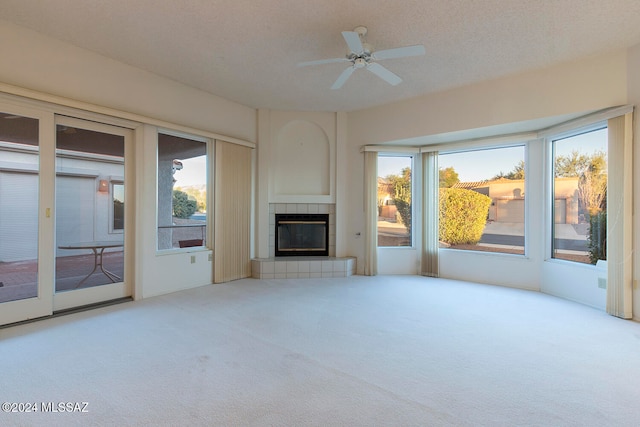 unfurnished living room with ceiling fan, a textured ceiling, a tile fireplace, and light colored carpet