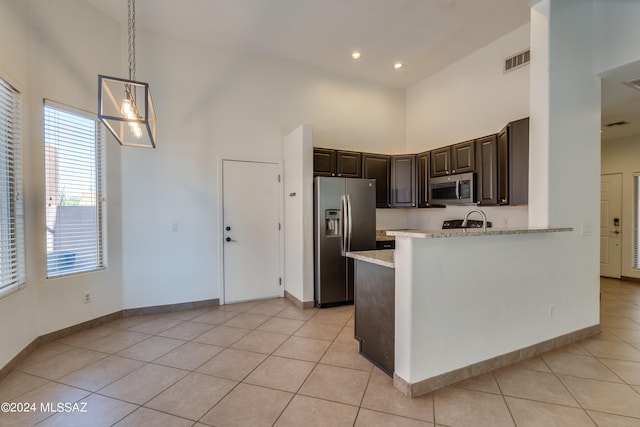 kitchen with light stone counters, high vaulted ceiling, kitchen peninsula, stainless steel appliances, and dark brown cabinets