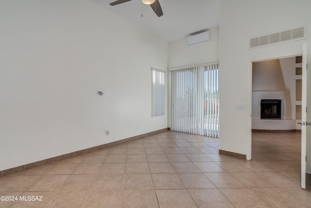 empty room with a fireplace, light tile patterned floors, a high ceiling, ceiling fan, and a wall unit AC