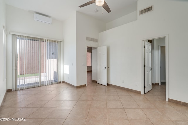 unfurnished bedroom featuring light tile patterned floors, access to exterior, a high ceiling, ceiling fan, and a wall mounted air conditioner