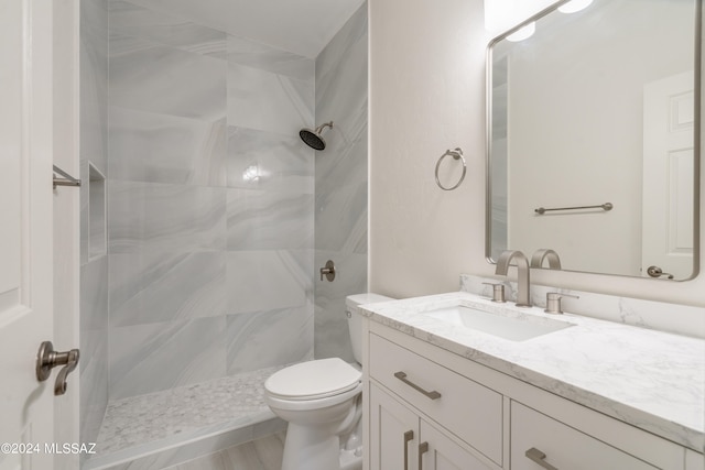 bathroom with a tile shower, vanity, and toilet