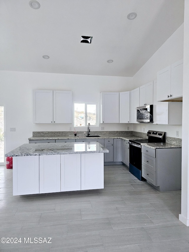 kitchen featuring a center island, appliances with stainless steel finishes, white cabinetry, a sink, and light stone countertops