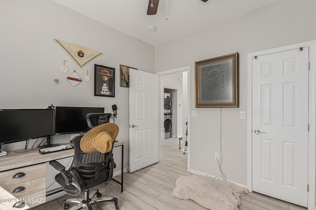 office area featuring ceiling fan, light wood-type flooring, and stacked washer / drying machine