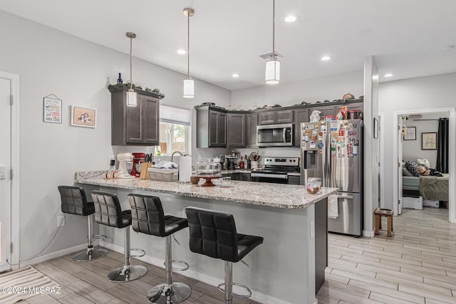 kitchen featuring kitchen peninsula, dark brown cabinets, decorative light fixtures, stainless steel appliances, and light hardwood / wood-style floors