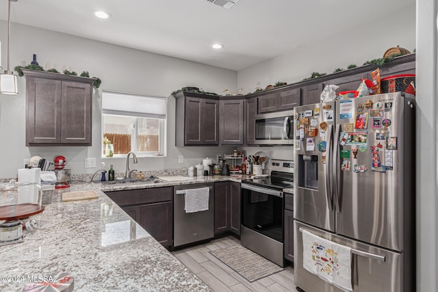 kitchen with light stone counters, pendant lighting, appliances with stainless steel finishes, and dark brown cabinets