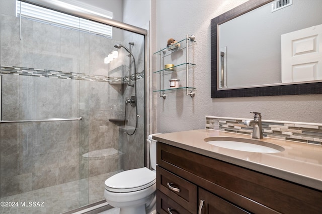 bathroom with toilet, vanity, decorative backsplash, and a shower with shower door