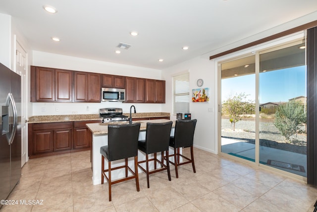 kitchen featuring appliances with stainless steel finishes, a breakfast bar, light stone counters, a center island with sink, and light tile patterned flooring