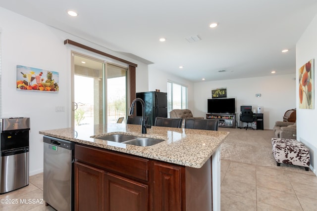 kitchen featuring light stone countertops, dishwasher, a kitchen island with sink, light tile patterned floors, and sink