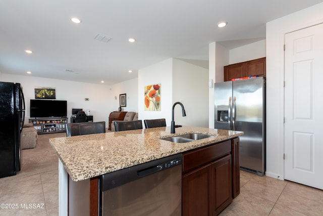 kitchen featuring appliances with stainless steel finishes, sink, a kitchen island with sink, light tile patterned flooring, and light stone counters