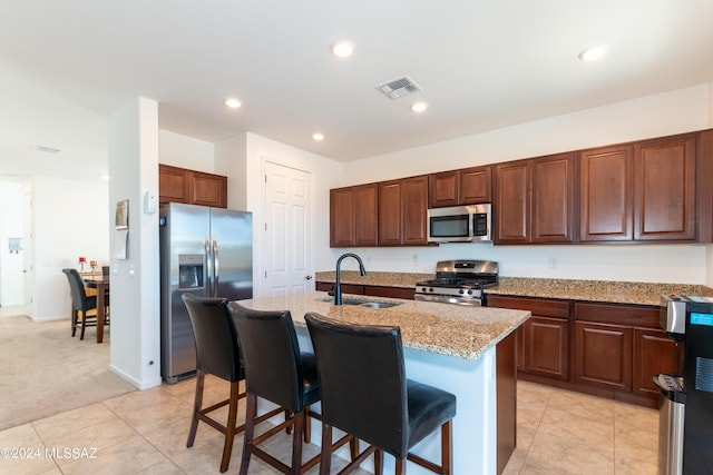 kitchen featuring sink, light colored carpet, a kitchen bar, a center island with sink, and stainless steel appliances