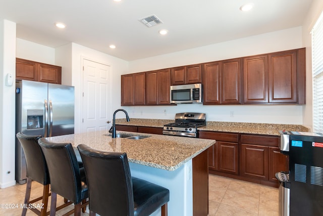 kitchen with a kitchen bar, light stone countertops, appliances with stainless steel finishes, sink, and a center island with sink