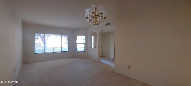 spare room featuring a chandelier and light colored carpet