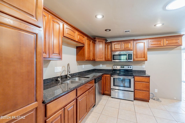 kitchen with dark stone countertops, appliances with stainless steel finishes, brown cabinetry, and a sink