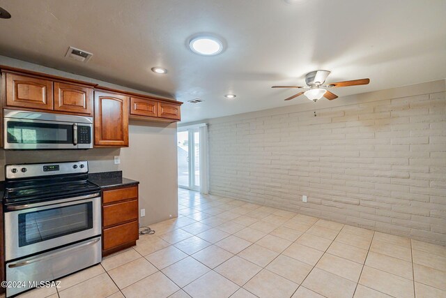 kitchen featuring brown cabinets, stainless steel appliances, brick wall, ceiling fan, and visible vents