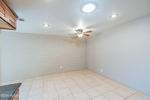 unfurnished room with light tile patterned floors, brick wall, visible vents, and a ceiling fan