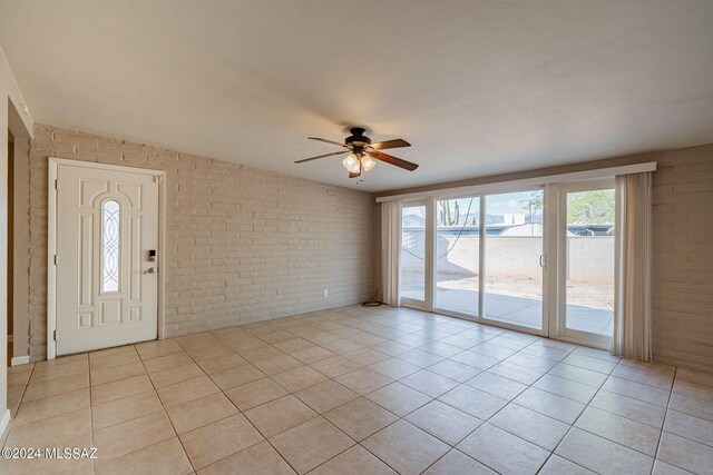 interior space with light tile patterned floors, ceiling fan, and brick wall