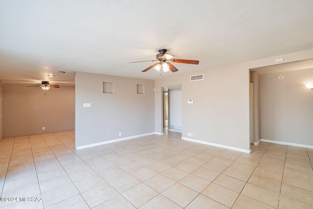 empty room featuring light tile patterned flooring, a ceiling fan, visible vents, and baseboards