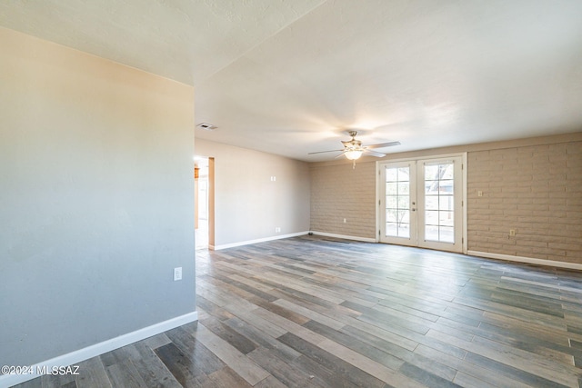 empty room with french doors, visible vents, brick wall, wood finished floors, and baseboards