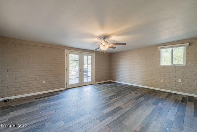 spare room featuring brick wall, a ceiling fan, baseboards, french doors, and dark wood-style floors