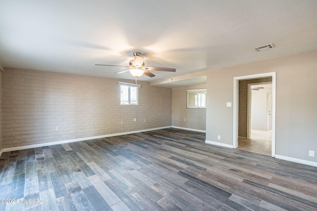 spare room with ceiling fan, brick wall, wood finished floors, visible vents, and baseboards