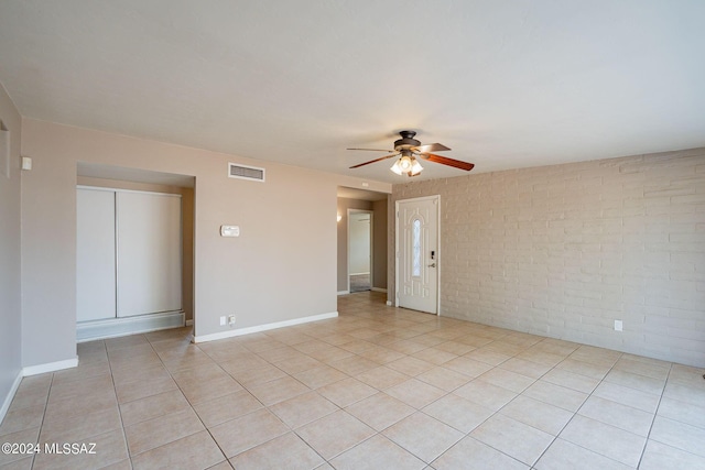 spare room with brick wall, light tile patterned floors, ceiling fan, visible vents, and baseboards