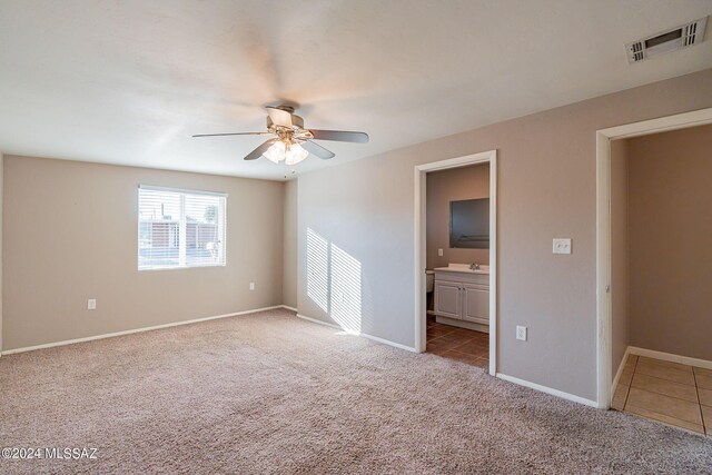 unfurnished bedroom with connected bathroom, light colored carpet, baseboards, visible vents, and a ceiling fan