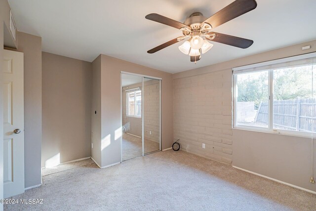 unfurnished bedroom featuring brick wall, a ceiling fan, carpet flooring, and a closet