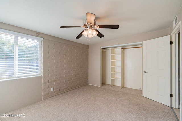 unfurnished bedroom with light carpet, brick wall, visible vents, a ceiling fan, and a closet