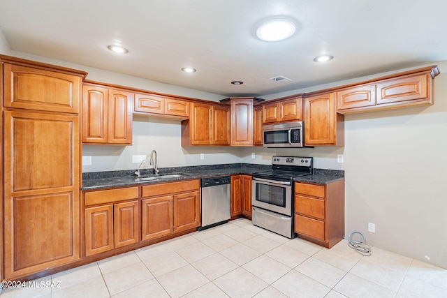 kitchen with stainless steel appliances, brown cabinetry, dark stone countertops, and a sink