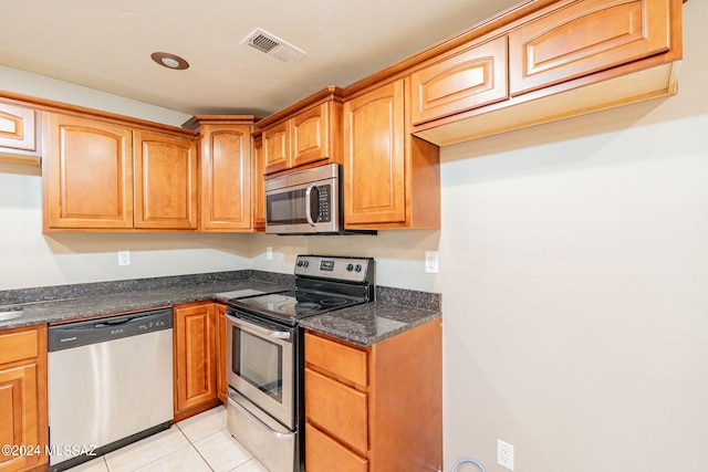 kitchen featuring light tile patterned floors, appliances with stainless steel finishes, dark stone counters, and visible vents