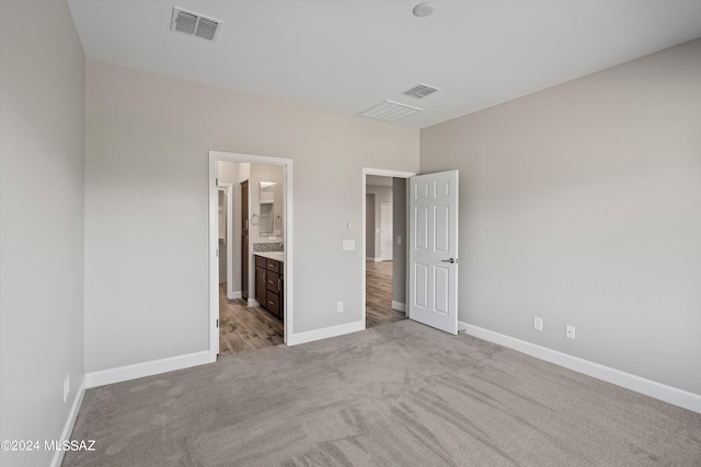 unfurnished bedroom with ensuite bath and light colored carpet