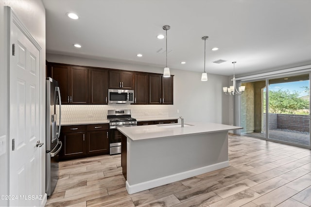 kitchen featuring a kitchen island with sink, sink, light hardwood / wood-style flooring, appliances with stainless steel finishes, and decorative light fixtures