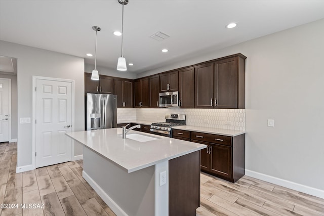 kitchen featuring appliances with stainless steel finishes, hanging light fixtures, light hardwood / wood-style floors, a kitchen island with sink, and sink