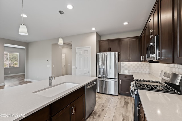 kitchen featuring sink, hanging light fixtures, light hardwood / wood-style flooring, decorative backsplash, and appliances with stainless steel finishes