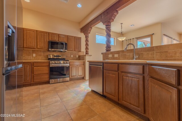 kitchen featuring light tile patterned flooring, decorative columns, hanging light fixtures, decorative backsplash, and appliances with stainless steel finishes