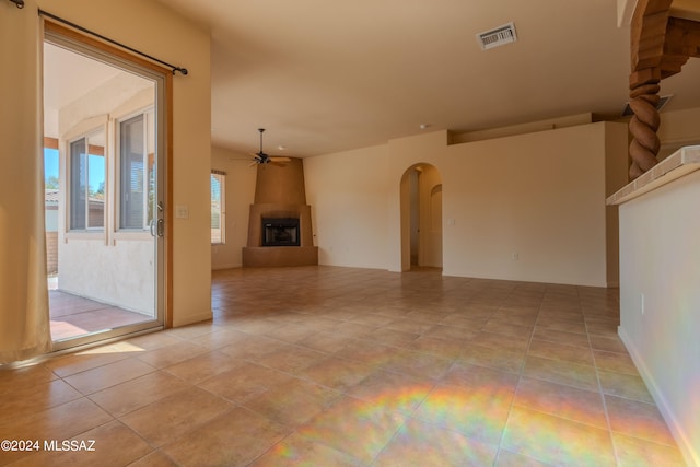 unfurnished living room featuring ceiling fan, light tile patterned flooring, and a large fireplace