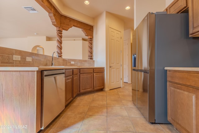 kitchen featuring appliances with stainless steel finishes, light tile patterned flooring, backsplash, beam ceiling, and sink