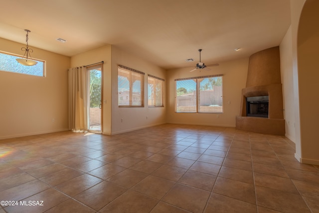 unfurnished living room featuring a healthy amount of sunlight, a fireplace, light tile patterned floors, and ceiling fan