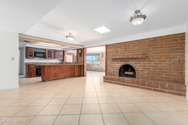 kitchen featuring a brick fireplace, kitchen peninsula, black appliances, light tile patterned floors, and brick wall