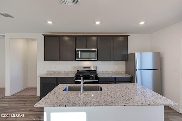 kitchen featuring an island with sink, sink, wood-type flooring, appliances with stainless steel finishes, and light stone countertops