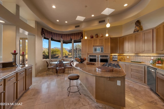 kitchen with decorative light fixtures, appliances with stainless steel finishes, a kitchen island, a towering ceiling, and light stone countertops