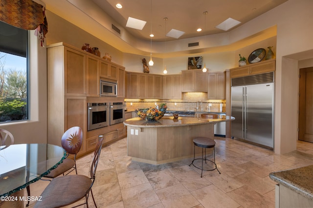 kitchen featuring a skylight, a center island, a high ceiling, built in appliances, and light brown cabinets