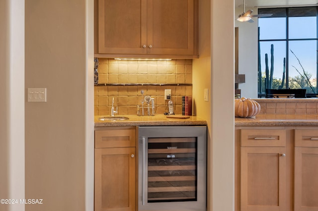 bar featuring light brown cabinetry, decorative light fixtures, tasteful backsplash, sink, and beverage cooler