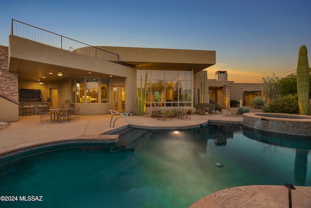 pool at dusk featuring a patio area and an in ground hot tub