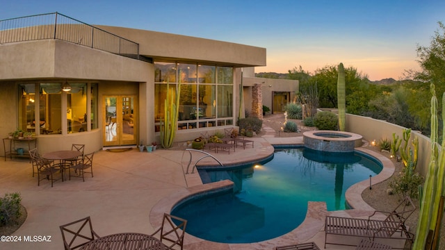 pool at dusk featuring an in ground hot tub and a patio area